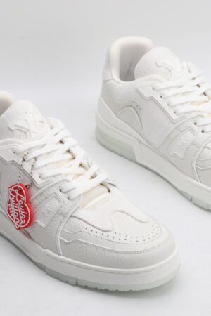 "A pair of PureEssence All-White Luxury Sneakers, viewed from an angle, showcasing their pristine low-top design, white laces, premium white leather upper with subtle textures, and a small red tag hanging from the left shoe