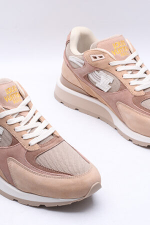 A pair of beige and light pink athletic sneakers made of mesh and suede, featuring white laces, a prominent logo on the side, and a thick, comfortable sole, with a brown "LOUIS VUITTON" shoebox in the background.