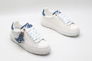 A single white Louis Vuitton Stellar Low-Top Sneaker, viewed from the side, featuring white leather, blue and white striped laces, and a blue denim heel tab.
