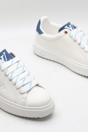 A single white Louis Vuitton Stellar Low-Top Sneaker, viewed from the side, featuring white leather, blue and white striped laces, and a blue denim heel tab.