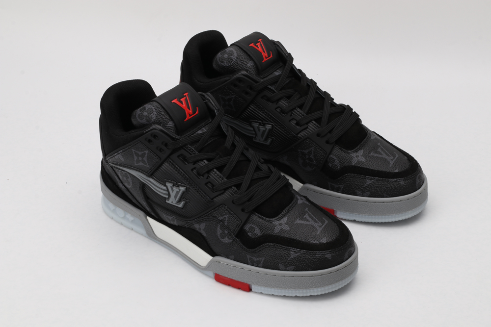 A pair of black and grey monogrammed low-top sneakers with red logo detailing on the tongue and a red accent on the outsole, featuring a white side logo and black laces, displayed against a light grey background.