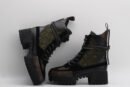pair of dark green quilted high-top boots with black leather and suede panels, brown monogram details on the toe and base, black laces, and a chunky black lug sole, displayed against a light grey background.