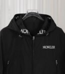 Black Moncler hooded nylon windbreaker jacket with white vertical Moncler logo tape detail along the front zipper and hood, shown on a hanger.