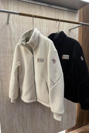 Close-up of a dark navy Moncler quilted jacket showing the brand's bell logo patch on the left shoulder and a high-quality zipper.