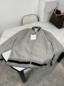 Silver or light grey Moncler nylon bomber jacket with horizontal red and blue stripes on the collar, cuffs, and hem, featuring a white Moncler logo patch on the chest
