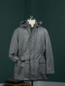 Grey herringbone wool parka with a hood and cinched waist on a mannequin, featuring a zip-front closure and a classic textured finish.