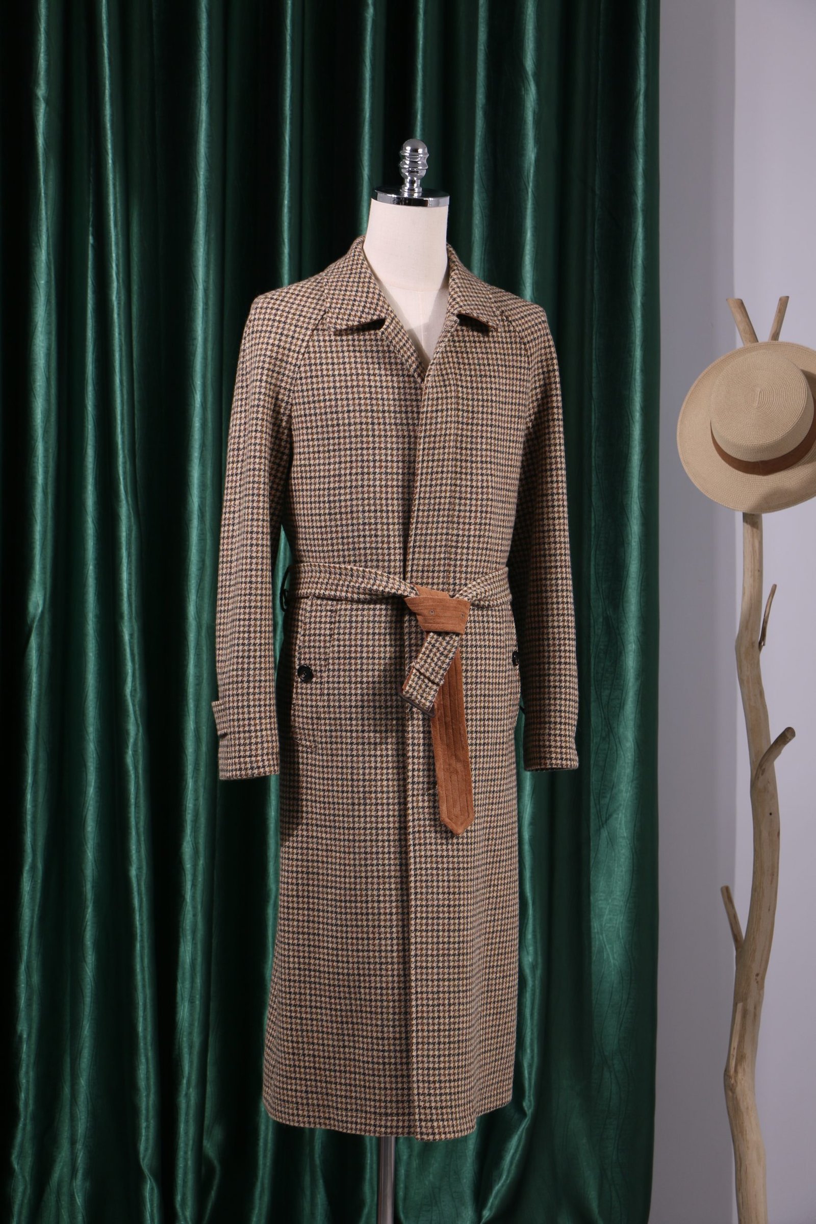 A long houndstooth patterned overcoat for men featuring a brown tipped waist belt and a classic collar on a mannequin.
