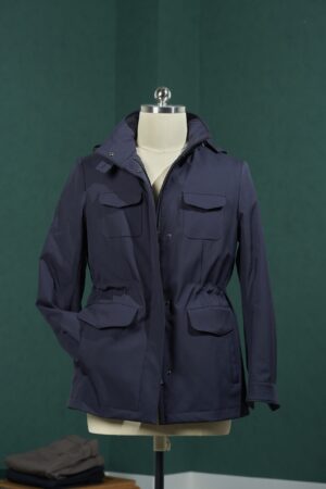 Dark navy Burberry style technical field jacket on a mannequin, featuring a high collar, four flap pockets, and a gathered elastic waist.