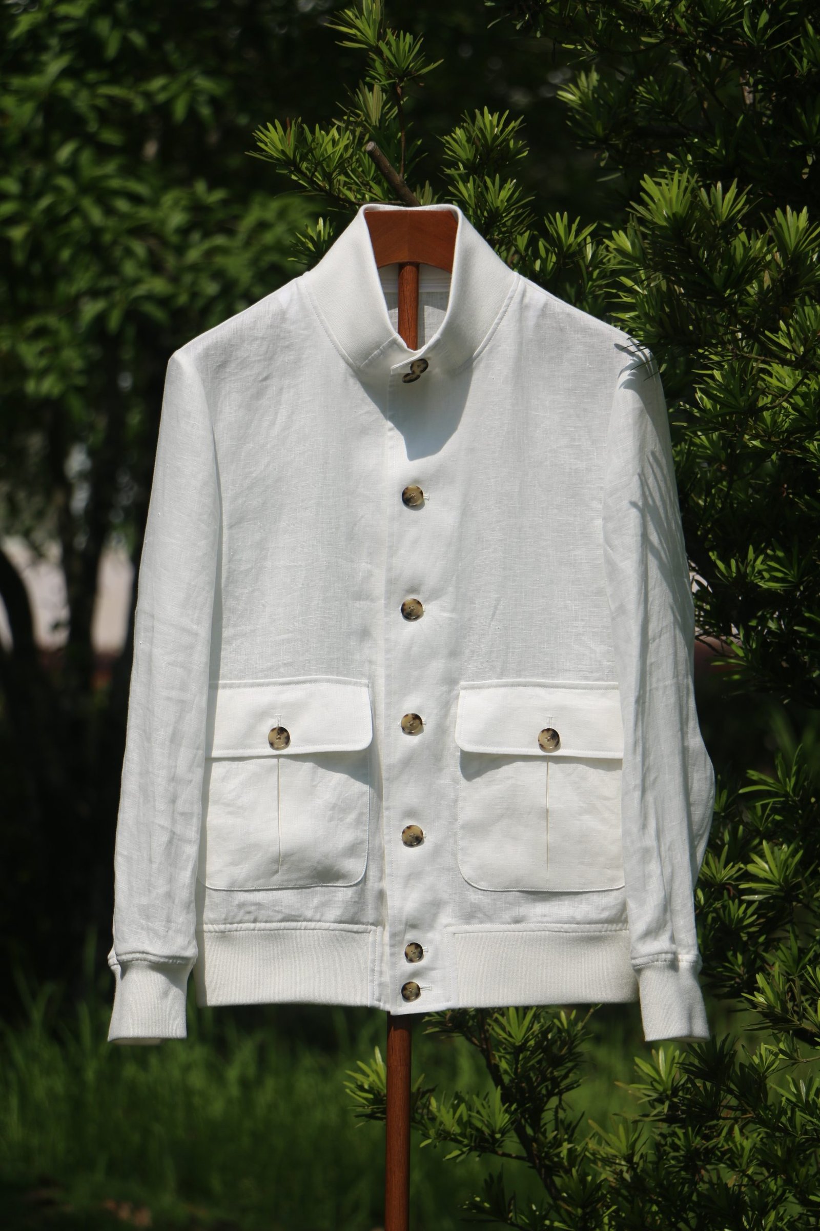 A crisp white Burberry linen jacket with ribbed cuffs and large front pockets hanging on a wooden stand outdoors.