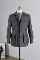 A charcoal grey textured wool safari jacket on a mannequin, styled with a striped shirt and grey tie.