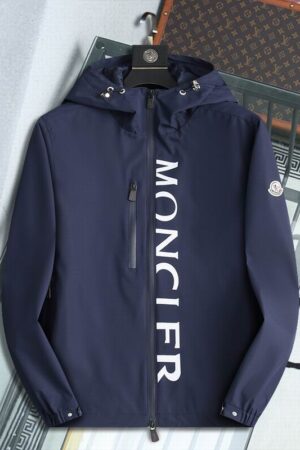 Navy blue hooded windbreaker jacket with white vertical lettering on the front, hanging on a black hanger against a modern interior background.