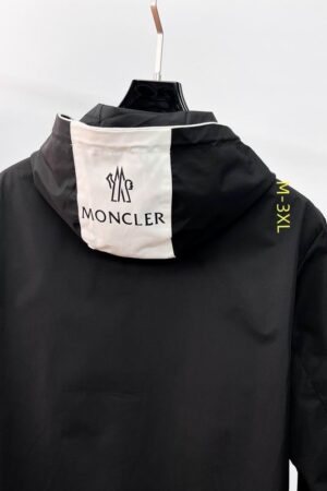 A premium black Moncler-inspired windbreaker featuring a signature tri-color striped trim on the hood, a zipped chest pocket, and a classic logo patch on the left sleeve utility pocket.