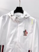 Close-up of a white Moncler Jofre windbreaker with a large embroidered chest logo, white drawstring hood, and red and blue striped zip pockets.