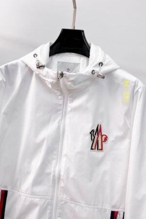 Close-up of a white Moncler Jofre windbreaker with a large embroidered chest logo, white drawstring hood, and red and blue striped zip pockets.