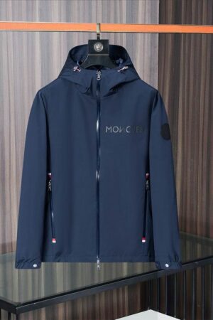 Navy blue Moncler soft-shell jacket with "MONCLER" printed on the chest, tricolor zip details, and a black logo patch on the left sleeve