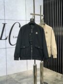 A black and a cream bomber jacket hanging on a silver rack, featuring a unique asymmetrical front flap and large square pockets.