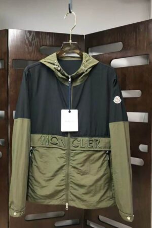 Two hooded Moncler style block-color jackets: one with a black upper half and olive green lower half, and one in solid black. Both feature a white patch logo and "MON CLER" lettering across the chest.
