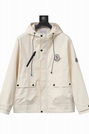 A cream-colored premium utility field jacket with two large front cargo pockets, a vertical chest zipper, and a signature logo patch on the chest.