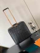 A luxury black quilted leather pilot suitcase with a gold telescopic handle and the iconic interlocking logo design standing on a black table.