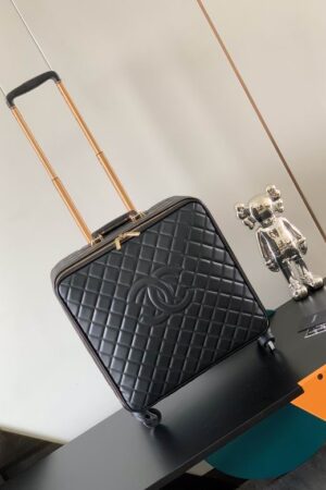 A luxury black quilted leather pilot suitcase with a gold telescopic handle and the iconic interlocking logo design standing on a black table.