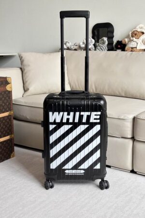 A modern matte black rolling suitcase with bold white diagonal stripes and branding stands in a minimalist room.