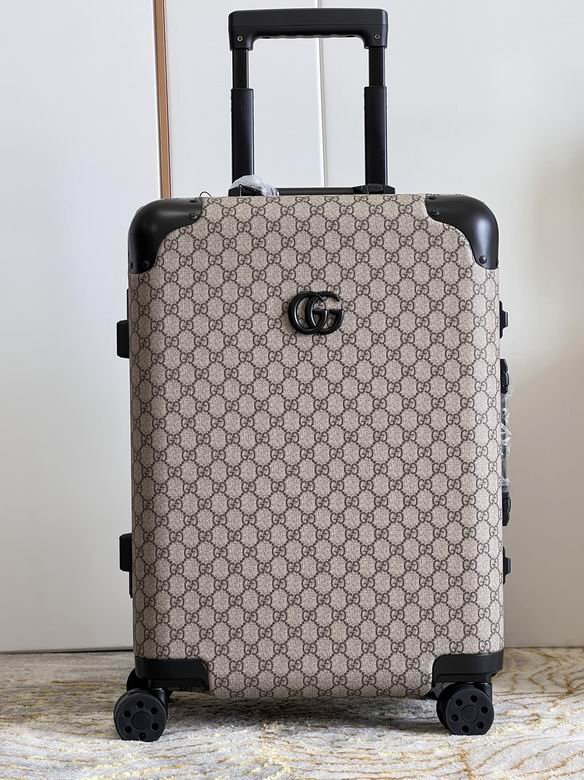 A beige and ebony Gucci GG Supreme rolling suitcase with black trim and a telescopic handle standing against a white wardrobe.