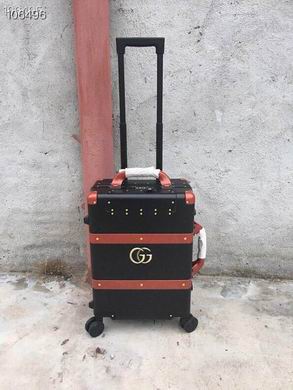 A black Gucci rolling suitcase with brown leather trim, a gold GG logo, and a telescopic handle standing against a concrete wall.