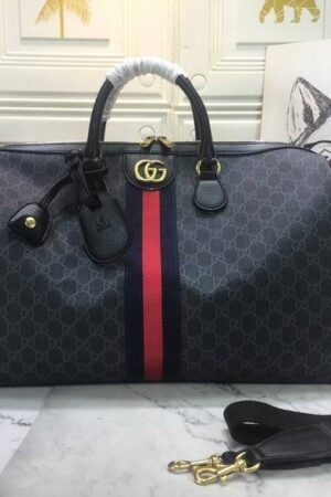 A Gucci Savoy duffle bag in black and grey GG Supreme canvas with a blue and red center stripe and gold GG logo on a marble table.