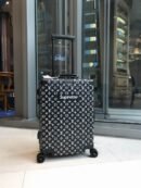 A black Louis Vuitton x Supreme cabin suitcase with white monogram print and a telescopic handle standing on a tiled floor.