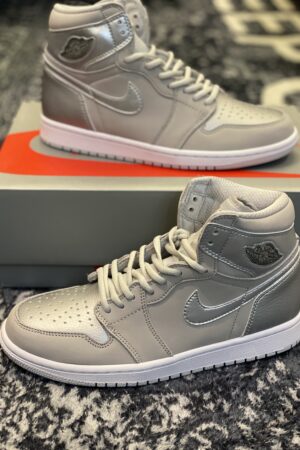 Top-down view of a pair of high-top sneakers in neutral grey leather with metallic silver accents on a patterned rug.