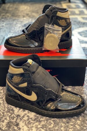 Front view of two shiny black and gold patent leather sneakers on a Nike box.