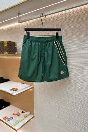 Moncler style green men's performance shorts with black and white side stripes hanging on a retail rack.