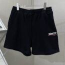 Black Balenciaga fleece shorts hanging on a metal rack, featuring a white embroidered 3B sports icon logo on the left thigh and an elastic drawstring waistband.