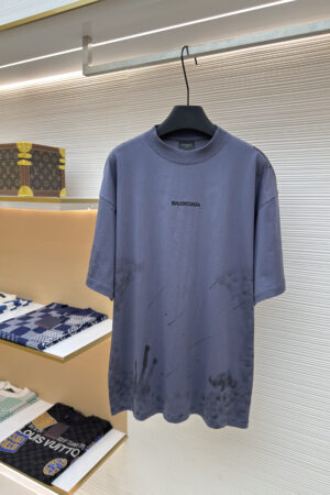 A dark grey short-sleeve T-shirt featuring a black Balenciaga logo and artistic dark mud-splatter distressing on the bottom.