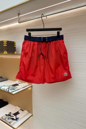 Vibrant red men's swim shorts with a navy blue waistband hanging on a display rack.