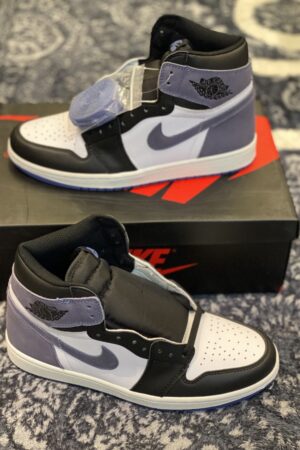 A pair of high-top sneakers with white leather, black overlays, and blue suede on the heel and swoosh resting on a black box.