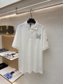 A crisp white men's pique polo shirt featuring a black-outlined varsity "M" on the chest and a designer sleeve patch hanging on a display rack.
