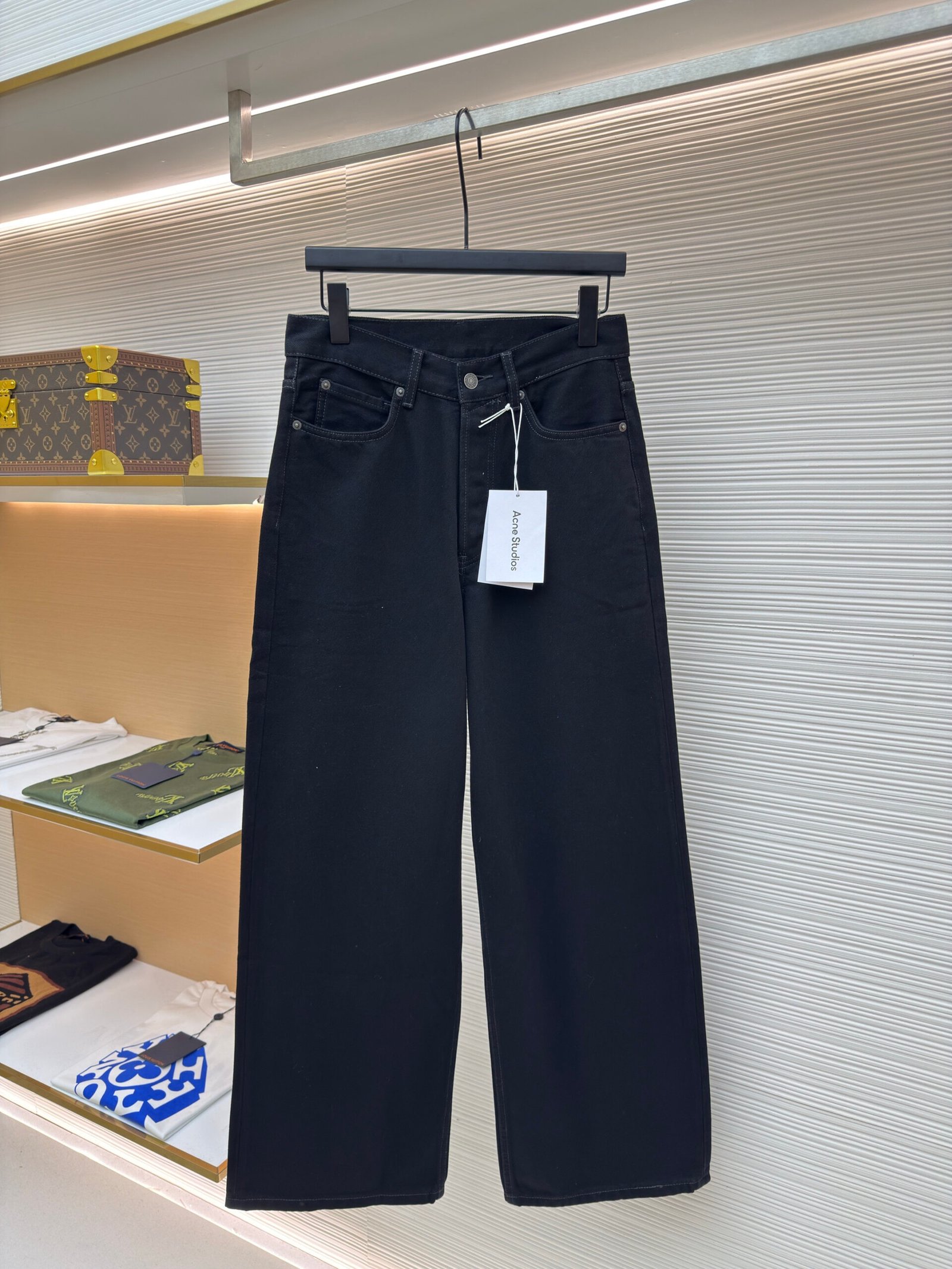 A pair of Acne Studios 1991 Toj loose-fit jeans in a clean black wash hanging in a luxury retail setting.