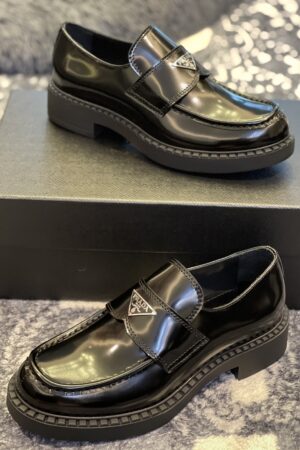 Close-up front view of black Prada brushed leather loafers with the silver triangle logo sitting on a black box.