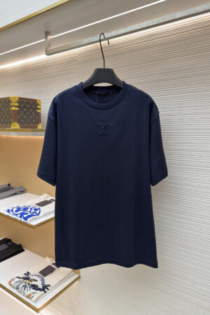 A premium men's navy blue cotton t-shirt featuring a tonal "LV" logo embroidered on the center chest hanging on a display rack.