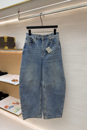 A pair of light blue wide-leg jeans by Loewe with a high-rise waist and distinctive knee seams, hanging on a black hanger in a luxury retail setting.