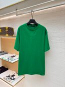 A premium men's emerald green cotton t-shirt featuring a tonal "LV" logo embroidered on the center chest hanging on a display rack.