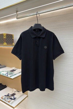 A premium black men's pique polo shirt featuring a tonal designer logo patch hanging on a display rack.