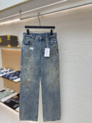 A pair of mid-blue Acne Studios distressed jeans with paint splatters and a loose fit hanging in a store.