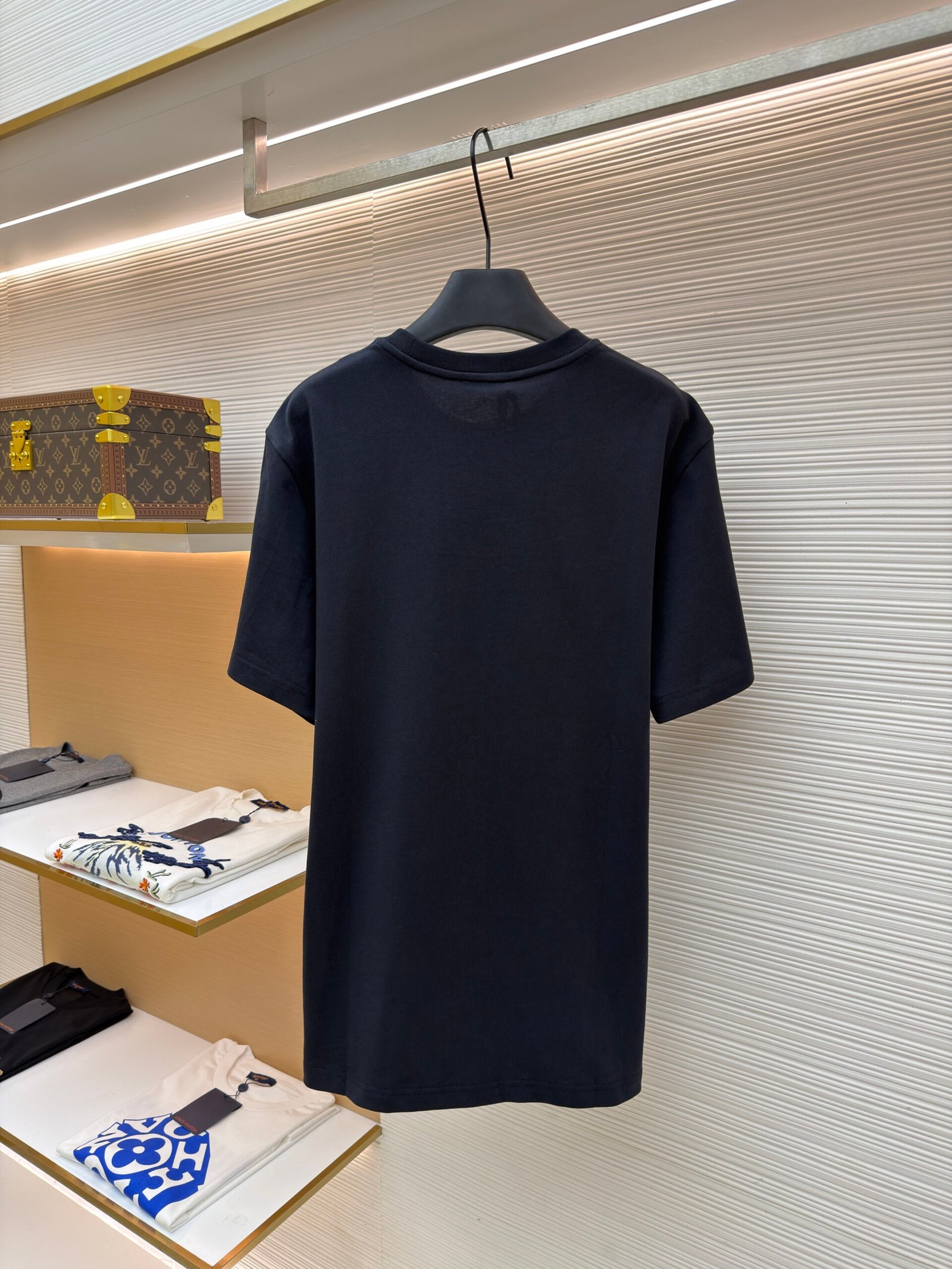 A deep navy blue men's cotton T-shirt featuring a unique triple-layered designer logo patch hanging on a display rack.