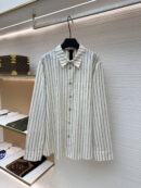 White long-sleeve button-down shirt with black vertical monogram stripes and silver floral buttons hanging on a rack.