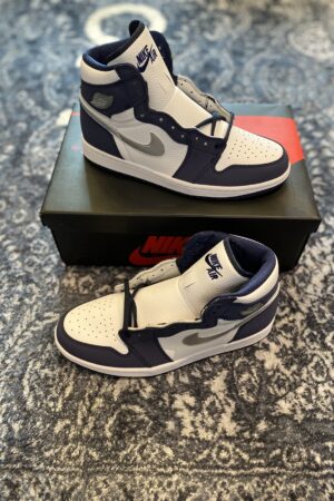 Two Midnight Navy and white Air Jordan 1 sneakers displayed on a black Nike shoe box.