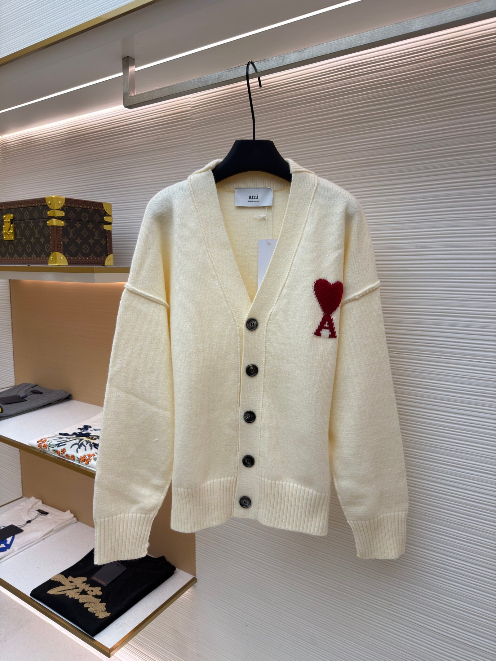A beige Saint Laurent long-sleeved canvas overshirt with a tonal embroidered YSL logo on the chest pocket, hanging on a black hanger in a luxury retail environment.