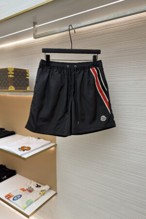 Men's black performance shorts with red, white, and navy side stripes hanging on a display rack.
