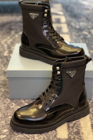 Side view of black Prada combat boots made of high-shine leather and matte nylon with the silver triangle logo sitting on a light blue box.